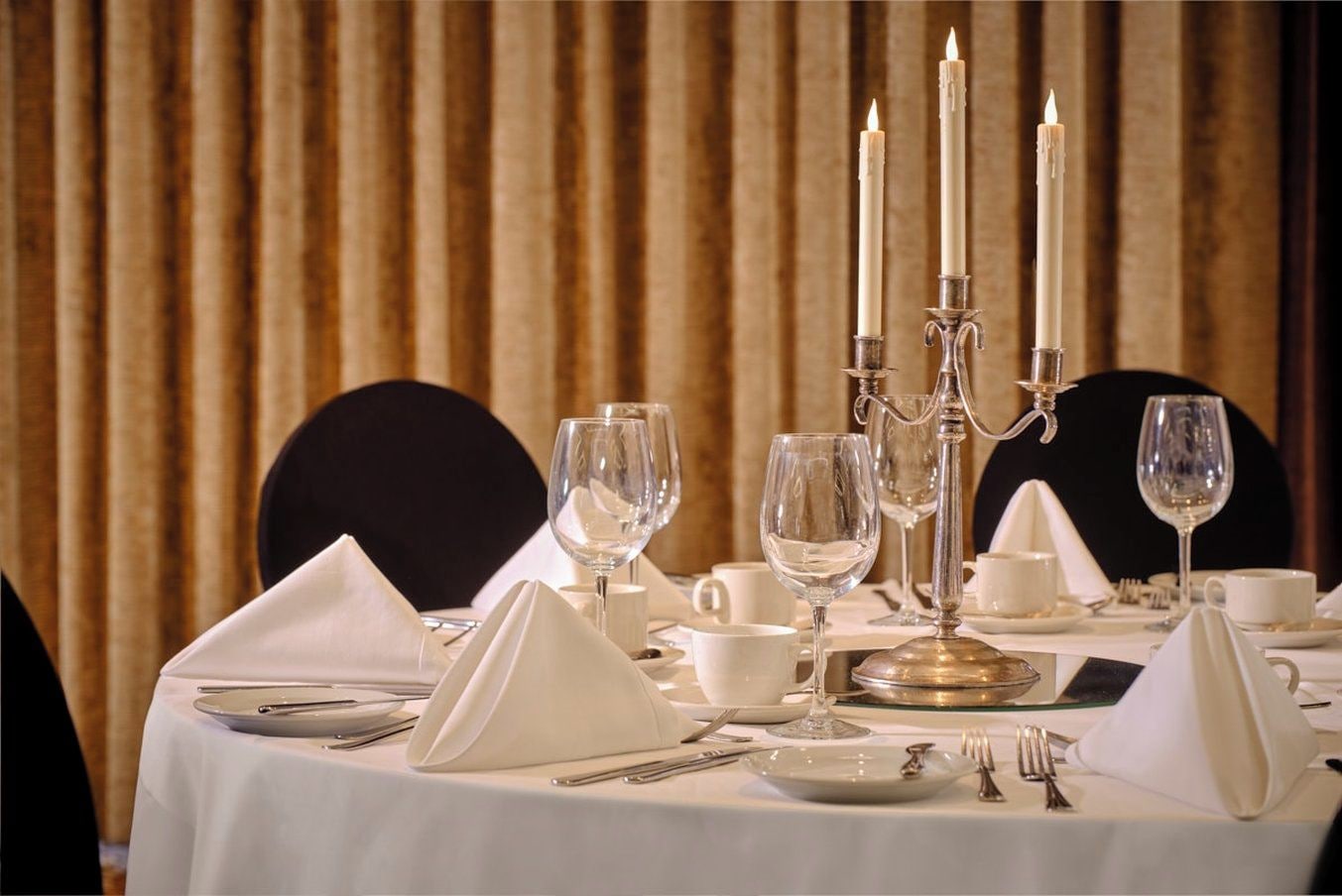 A table set for dining with white tablecloth, silverware, and wine glasses.