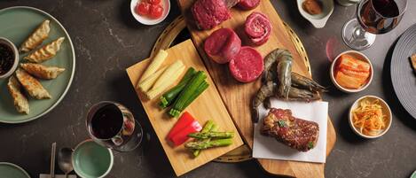 A variety of food items including dumplings, corn, asparagus, and meat on a wooden board, accompanied by small bowls of sauces and condiments.
