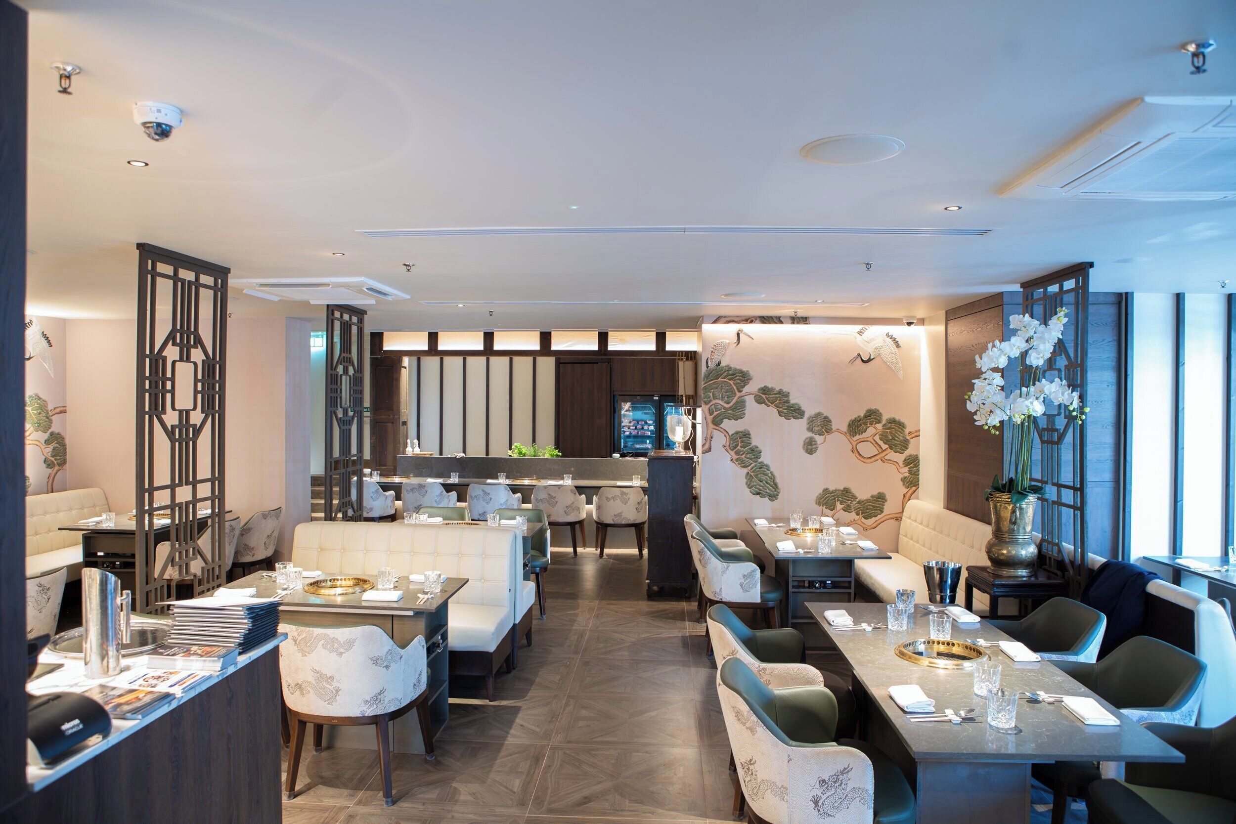 A modern restaurant with a central bar, multiple dining areas, and a decorative wall mural.