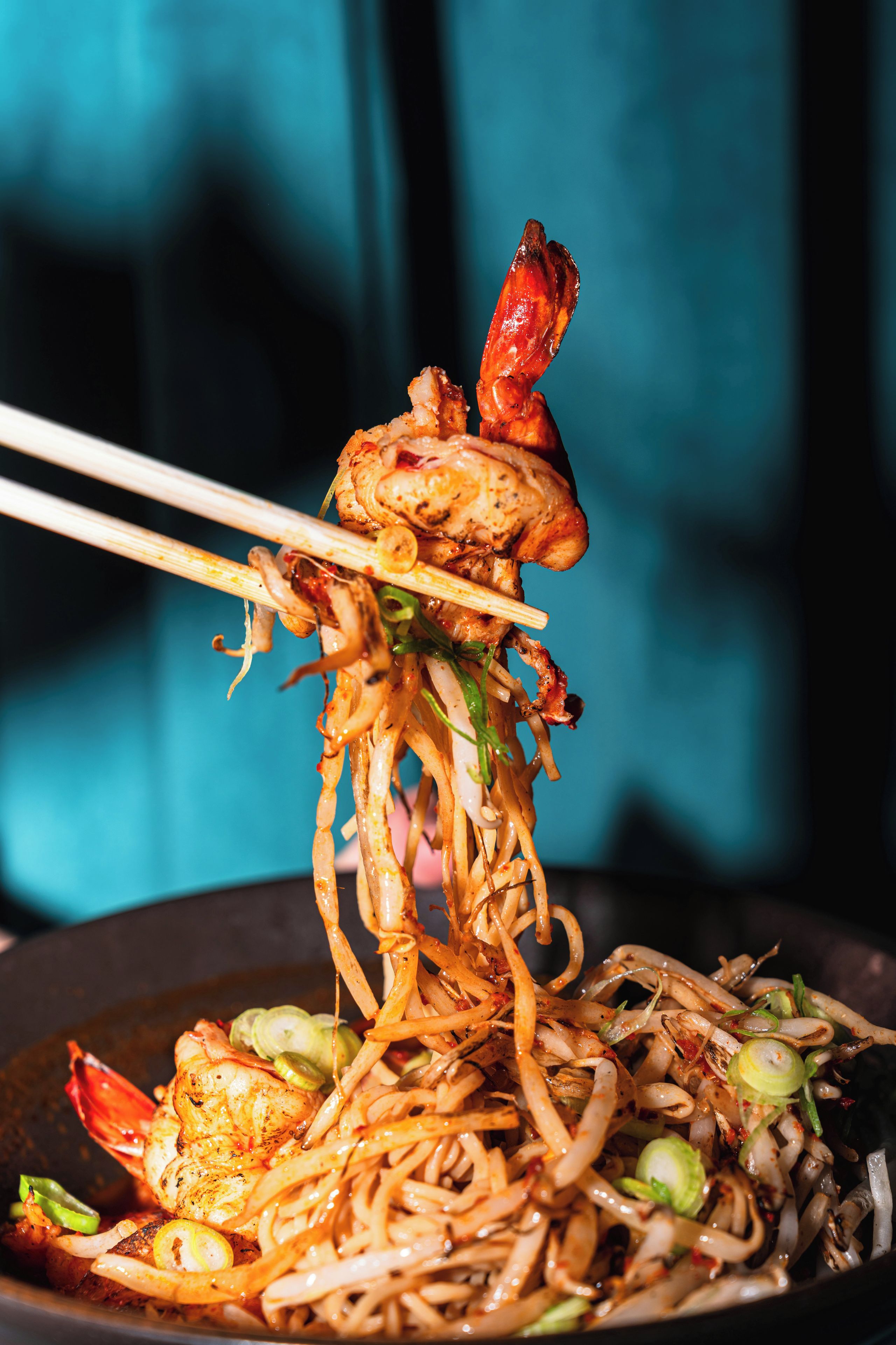 Un tazón de fideos con verduras y un cangrejo cocido, sostenido con palillos.