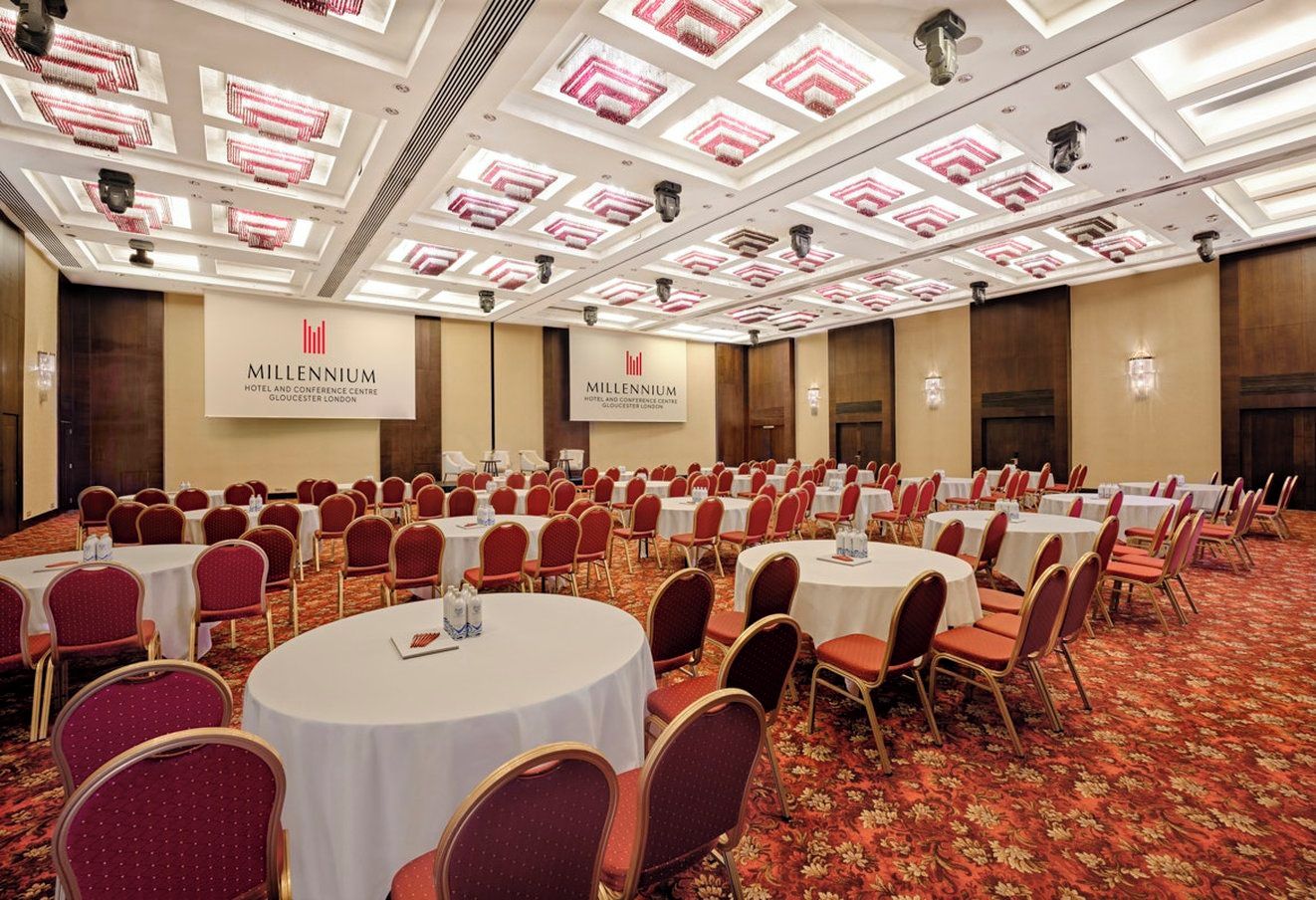 A conference room with round tables and red chairs, a carpeted floor, and a ceiling with patterned lights.