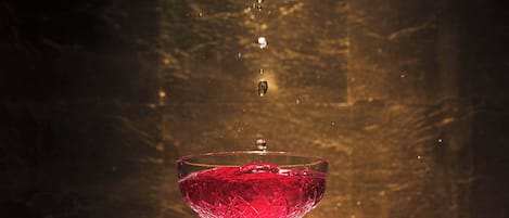 A clear glass with a red liquid, possibly a cocktail, with water droplets falling into it.
