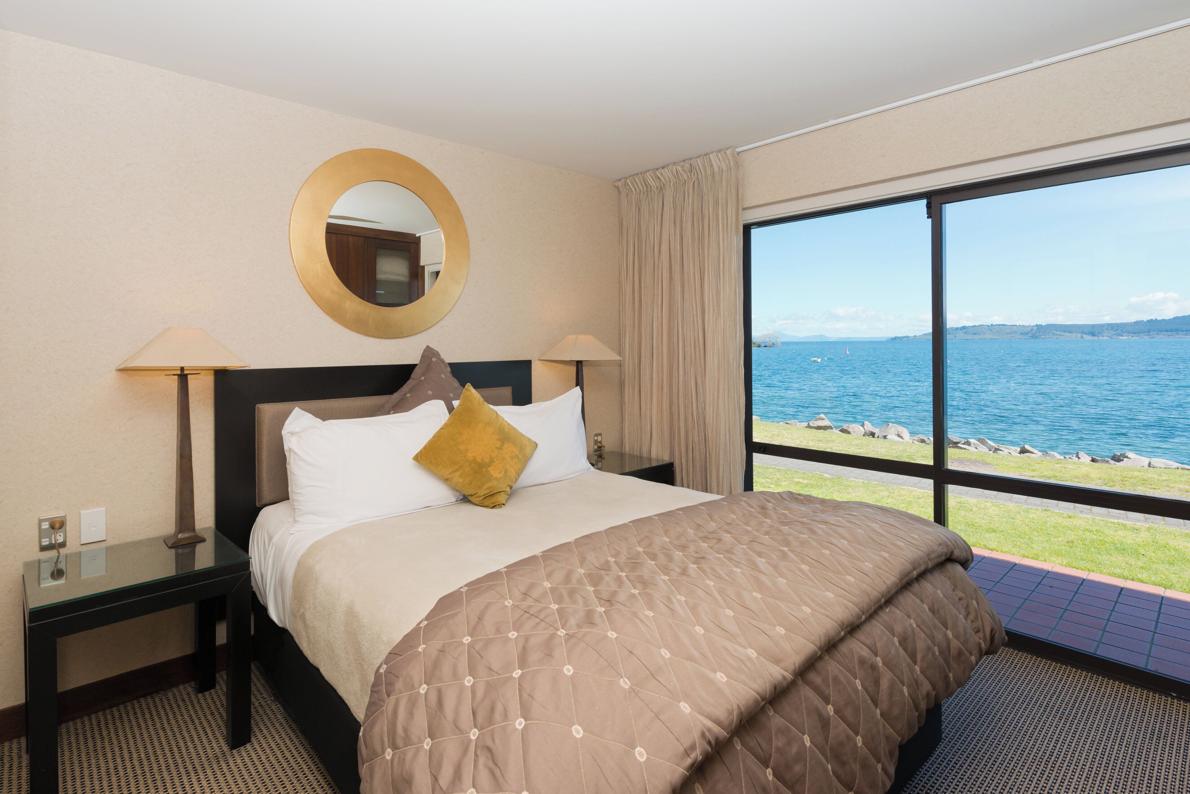 Een hotelkamer met een groot bed, een nachtkastje, een spiegel en uitzicht op zee.