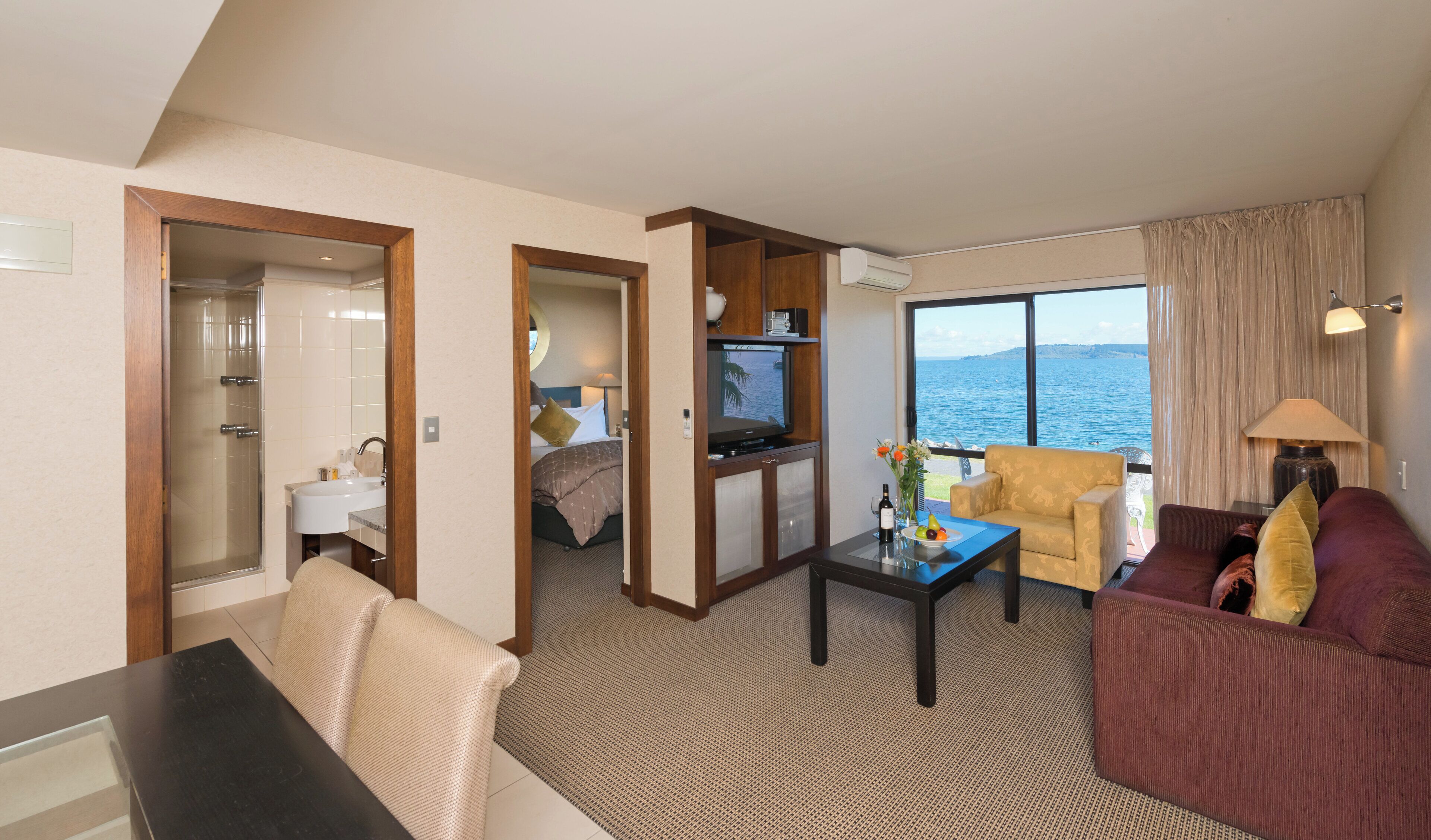 A hotel room with a bed, a television, a coffee table, and a view of the sea.