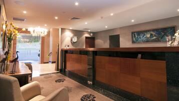 A hotel reception area with a wooden reception desk, a clock, and a painting on the wall.