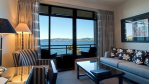 Habitación de hotel moderna con un amplio ventanal que ofrece vistas al mar, un sofá con cojines estampados, una mesa y una lámpara.