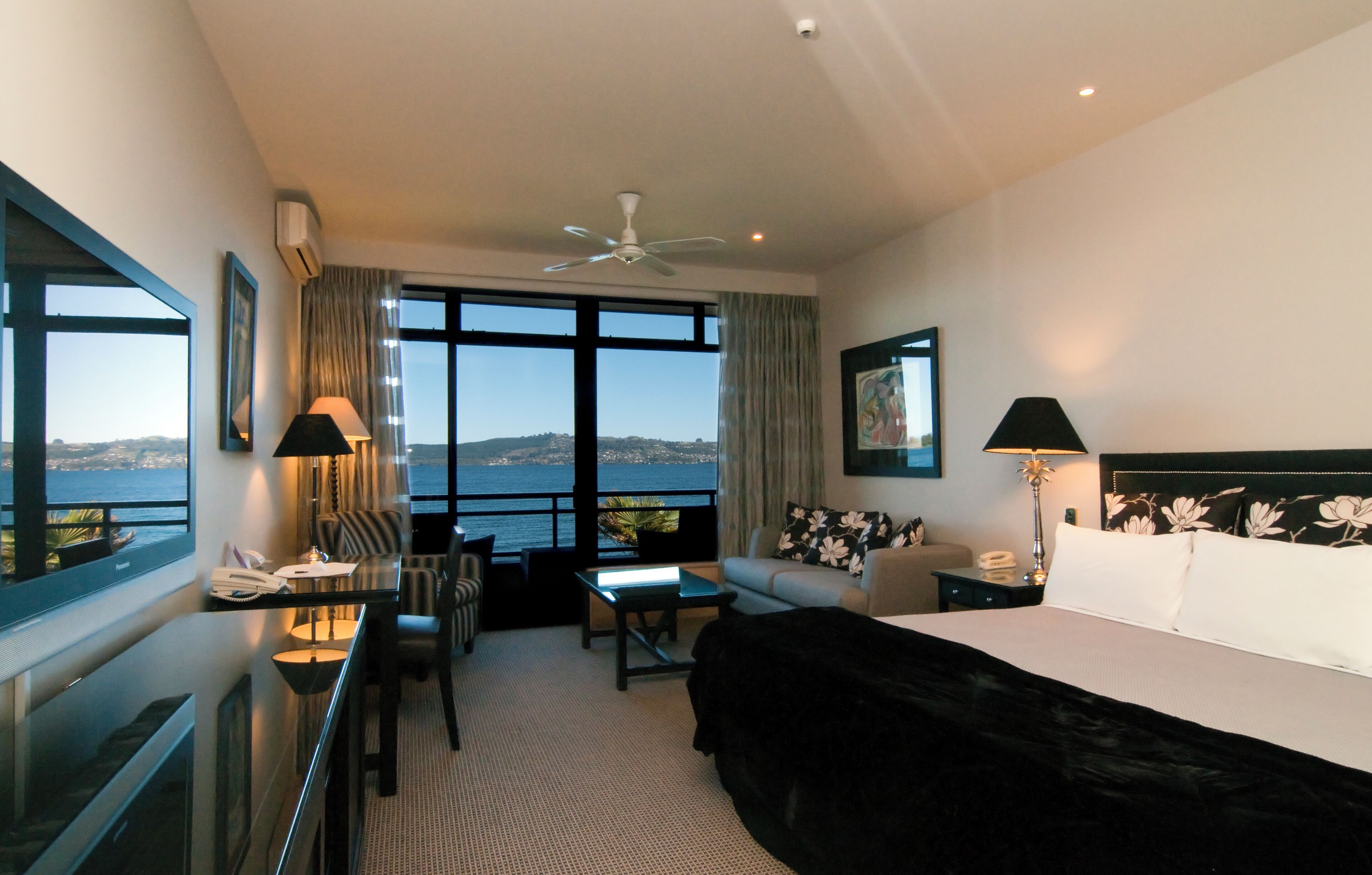 A hotel room with a bed, a desk, a chair, a sofa, and a view of the sea.