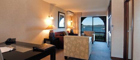 Habitación de hotel con escritorio, sofá, silla y vista al mar a través de un amplio ventanal.