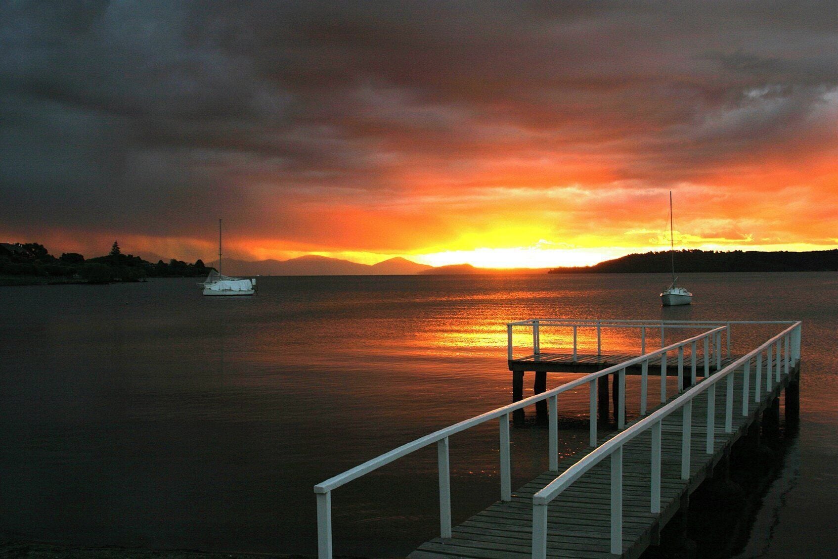 A sunset over a calm body of water with a dock extending into the water.