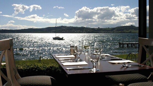 Mesa lista para comer con vista a un lago y un barco a lo lejos.