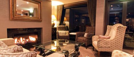 A cozy living room with a fireplace, patterned furniture, and a glass coffee table.