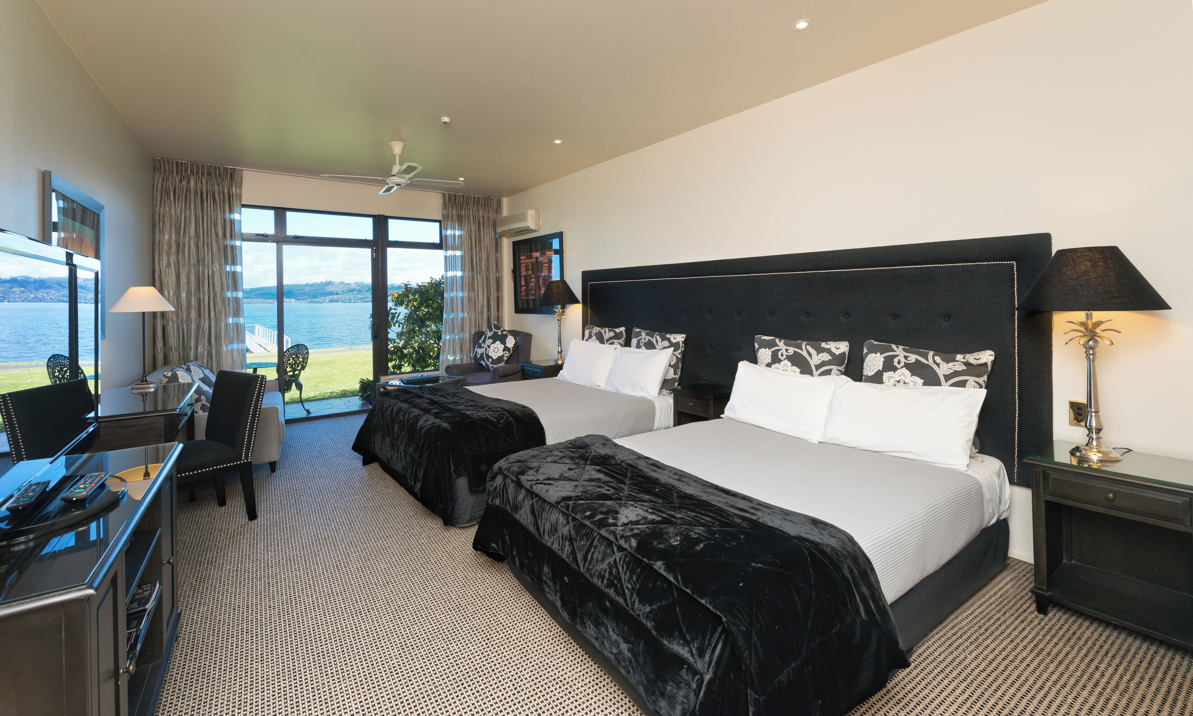 Habitación de hotel con dos camas, un escritorio y una silla. Amplia ventana con vista al mar.