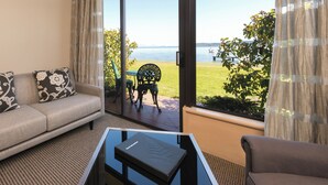 Una sala de estar con sofá, dos sillones, una mesa de centro de vidrio y vistas a un lago con muelle y bote.