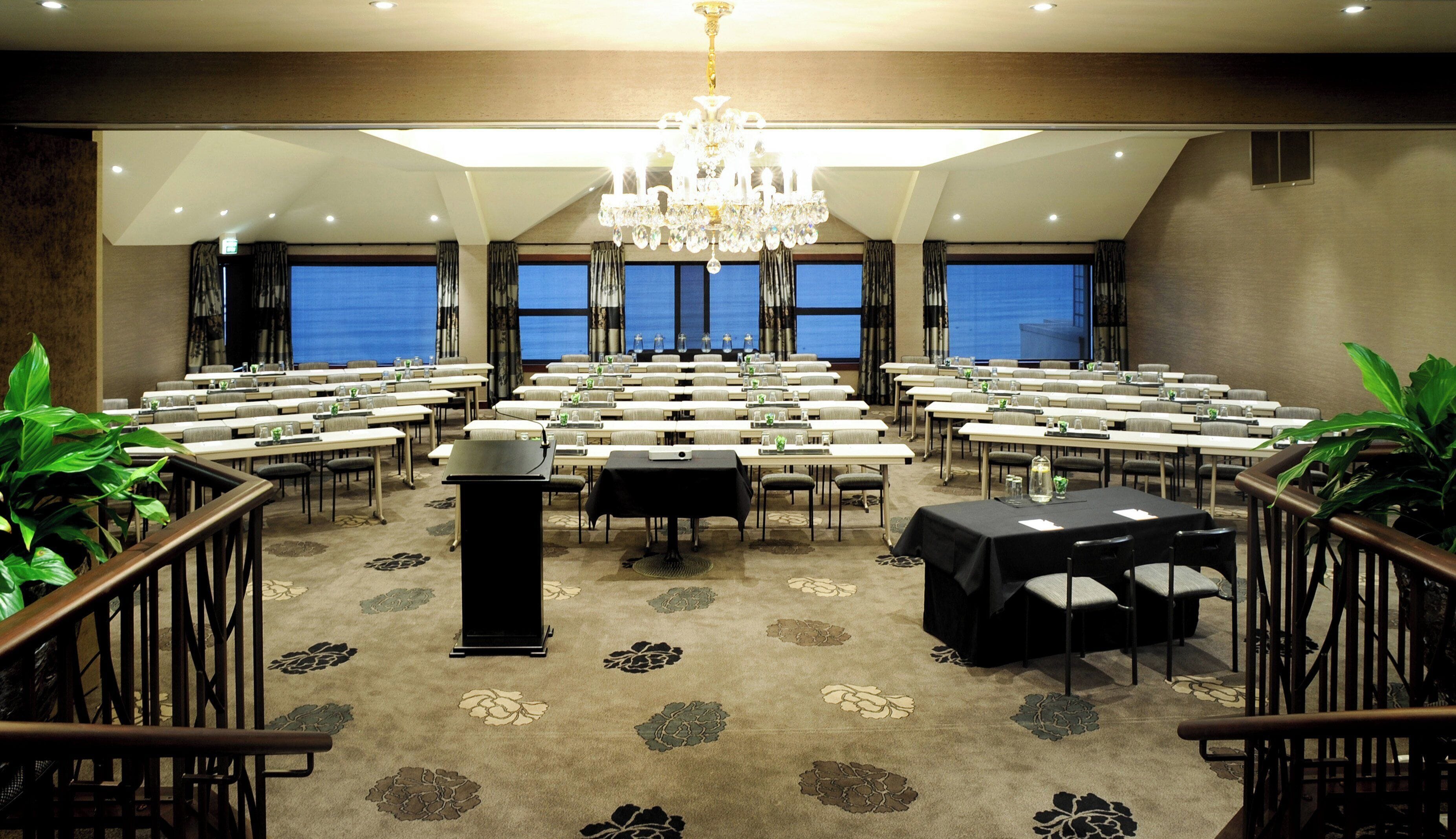 A conference room with rows of tables, a podium, and a chandelier.