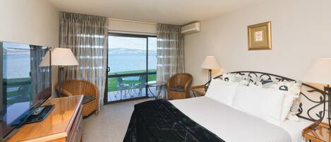 Ein Hotelzimmer mit einem Bett, zwei Stühlen, einem Schreibtisch mit Computer und einem großen Fenster mit Meerblick.