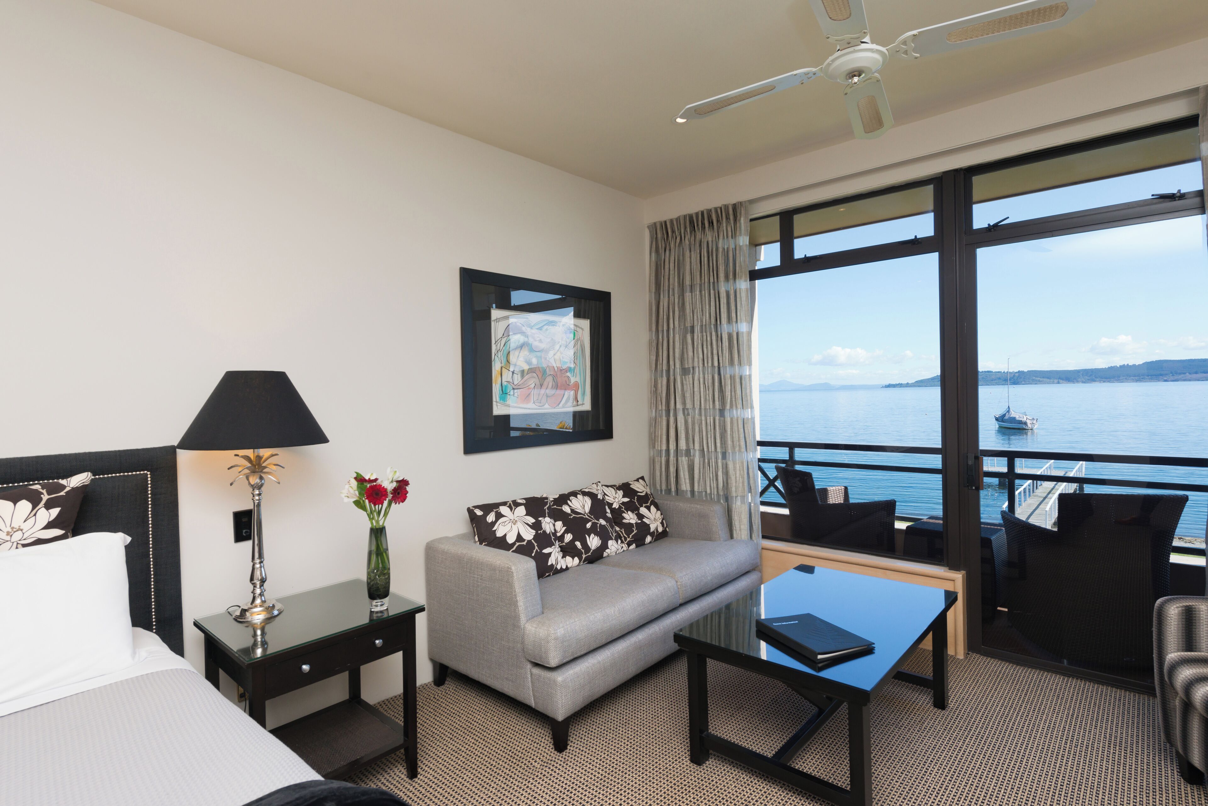 A hotel room with a bed, a sofa, a coffee table, a desk, and a view of the sea.