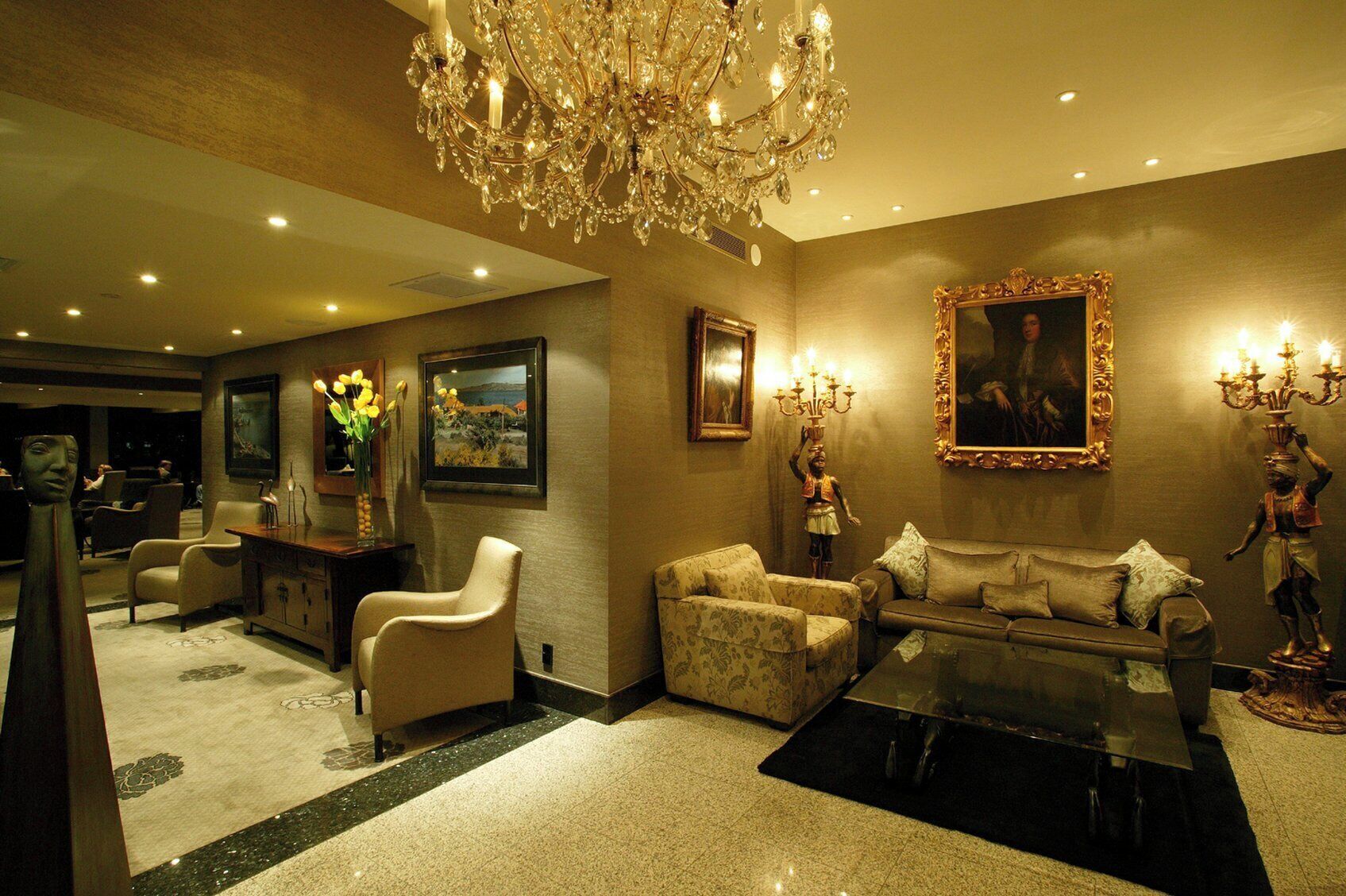 A luxurious living room with a chandelier, comfortable seating, and artwork on the walls.