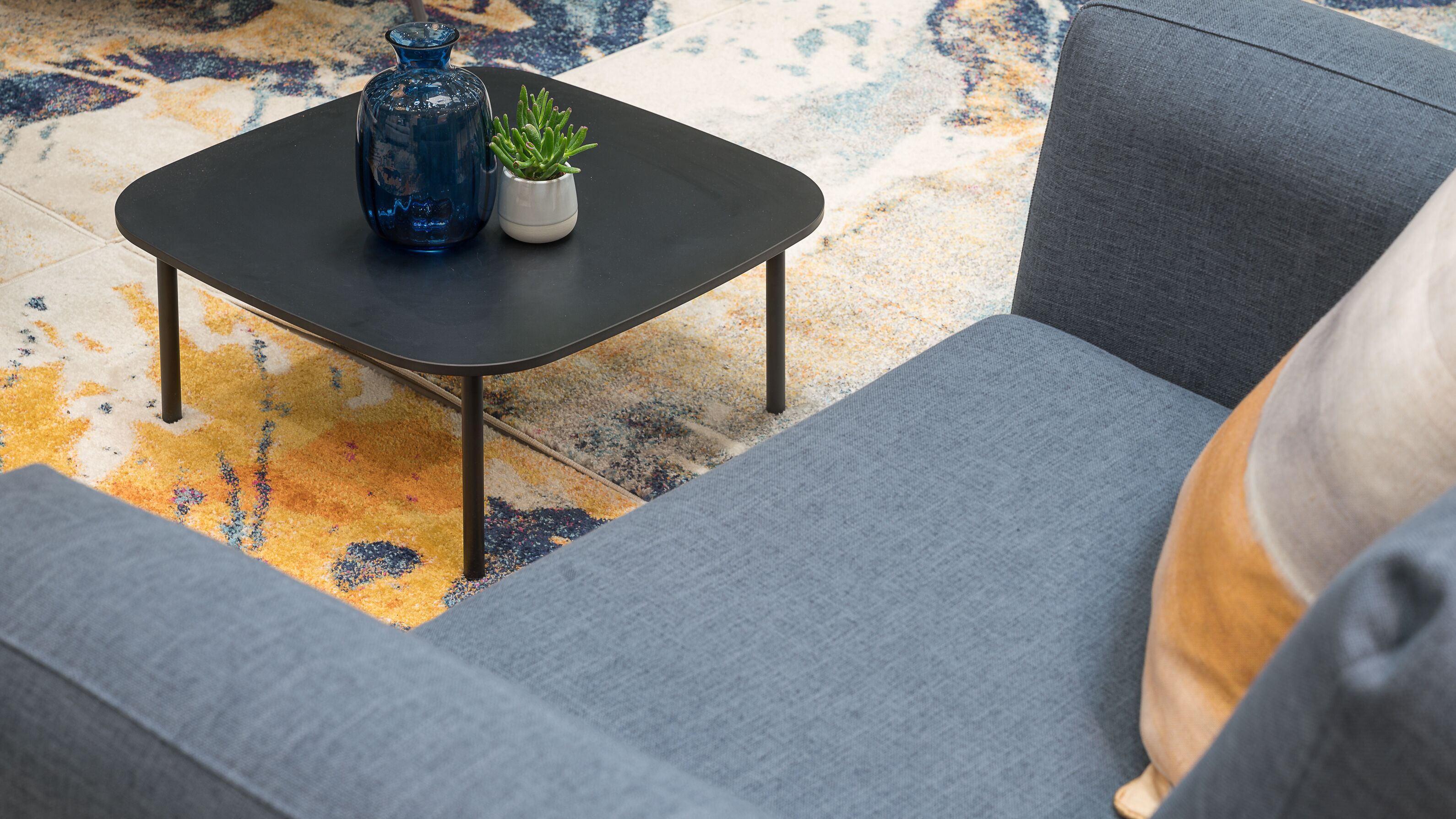 A modern living room with a grey sofa, a black coffee table, and a blue vase with a small plant.