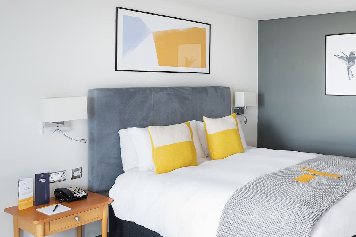 A modern hotel room with a large bed, bedside tables, a desk, and artwork on the walls.