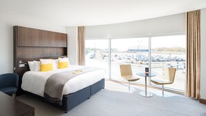 A hotel room with a large bed, a desk, two chairs, and a view of a parking lot.