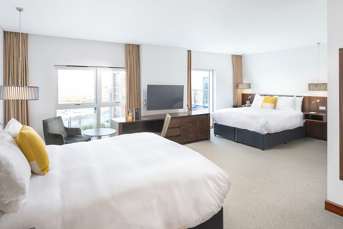 A hotel room with two beds, a desk, a TV, and a large mirror.