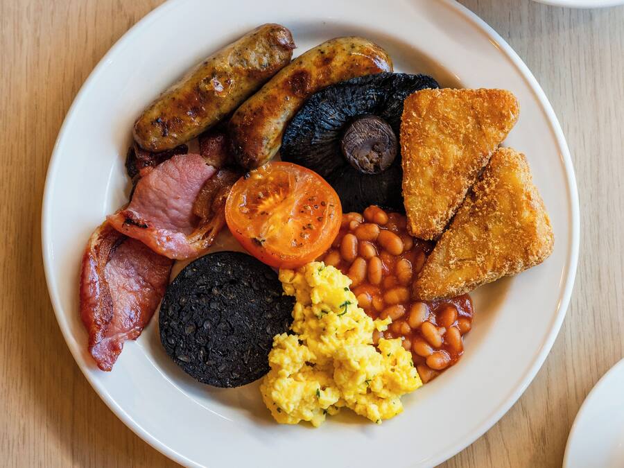 A plate of breakfast food including sausages, eggs, tomatoes, beans, and toast.