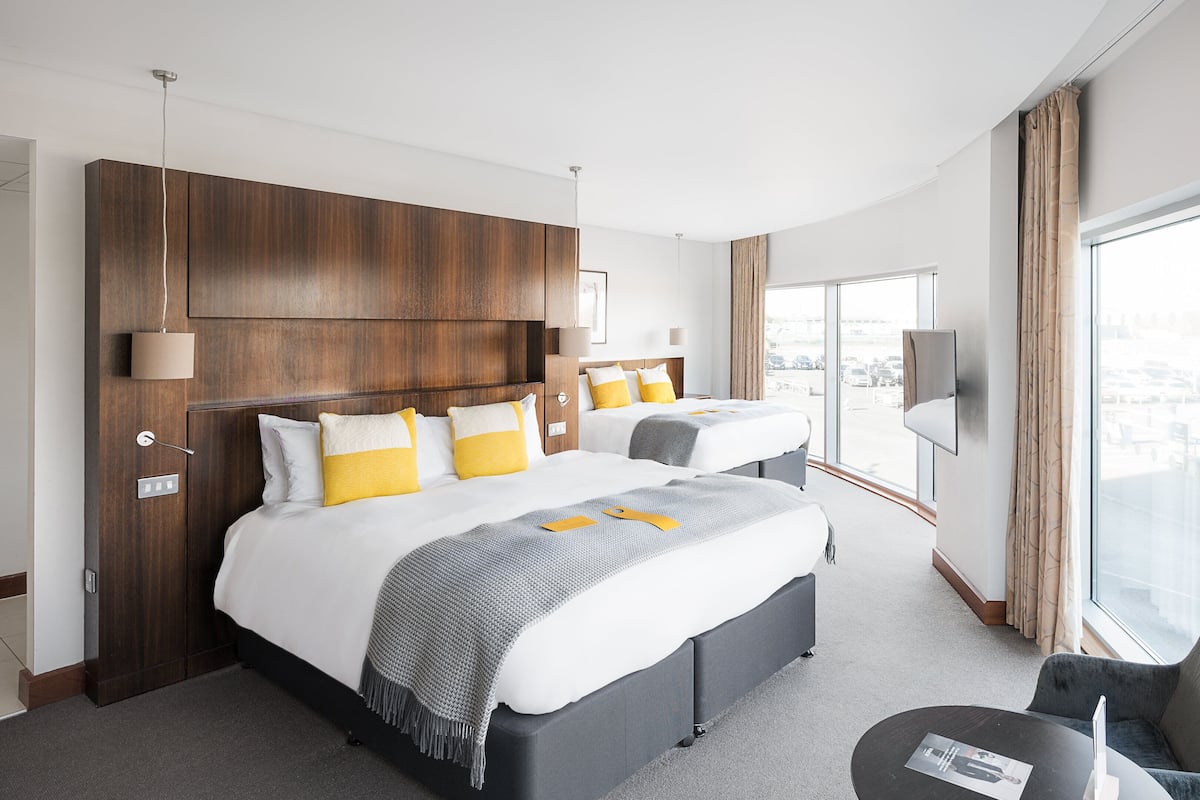 A hotel room with a large bed, a smaller bed, a desk, a chair, and a TV.