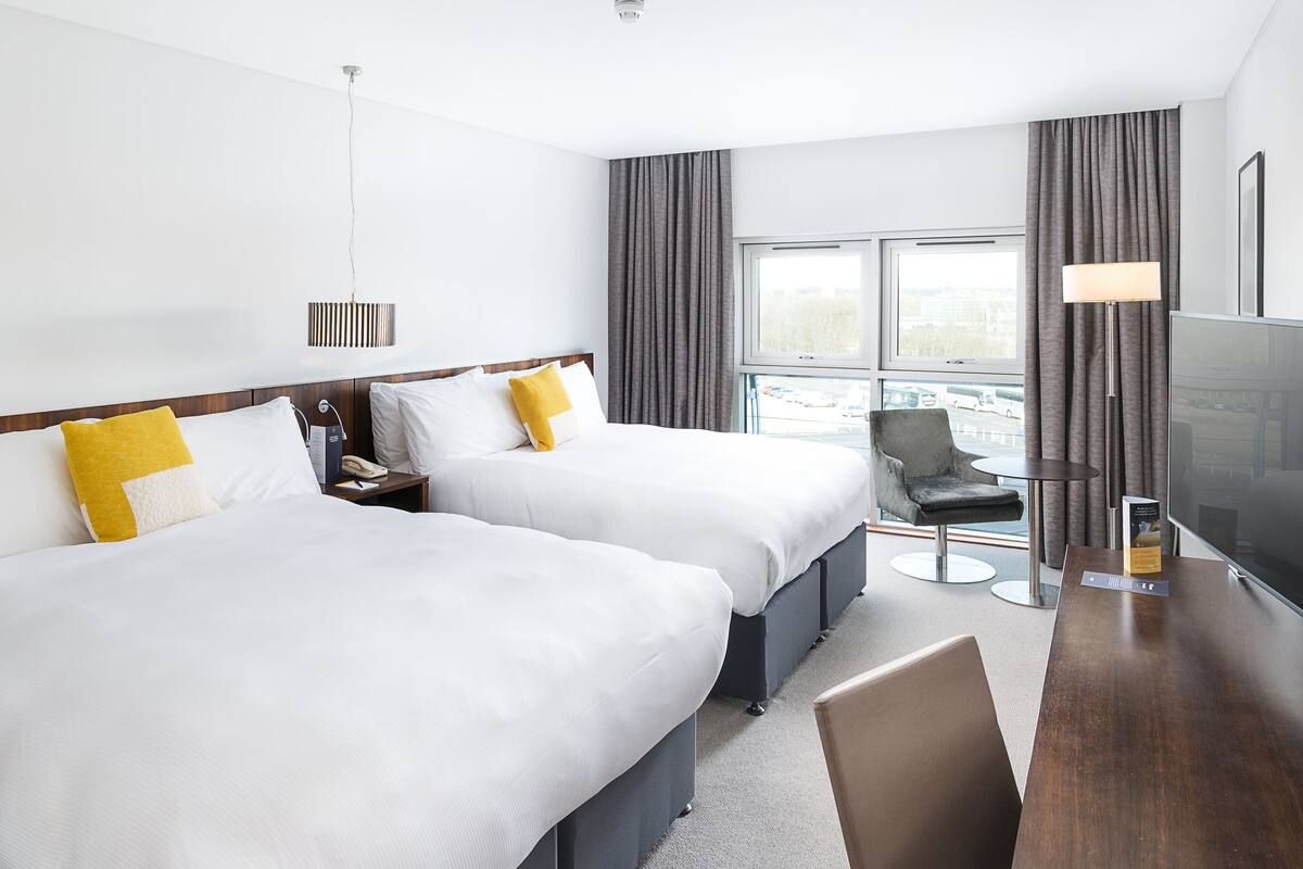 A hotel room with two beds, a desk with a chair, a TV, and a window with curtains.
