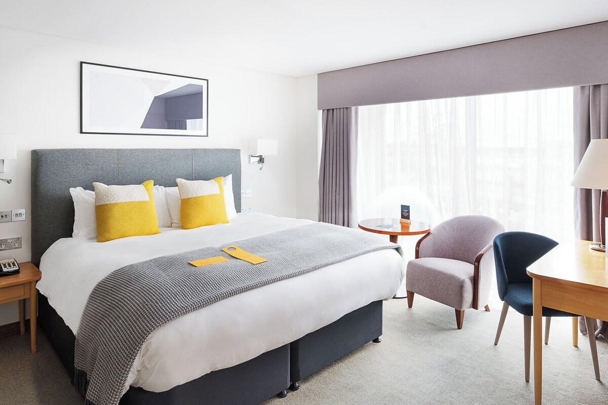 Una habitación de hotel con una cama grande, un escritorio, una silla y una ventana con cortinas.