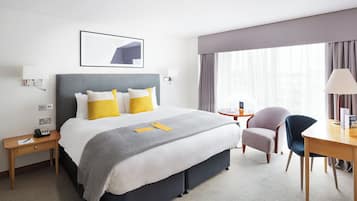 Una habitación de hotel con cama, mesitas de noche, escritorio, silla y ventana con cortinas.