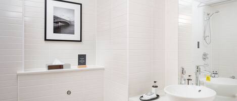 A modern bathroom with white tiled walls, a framed photograph, a sink, and a shower.