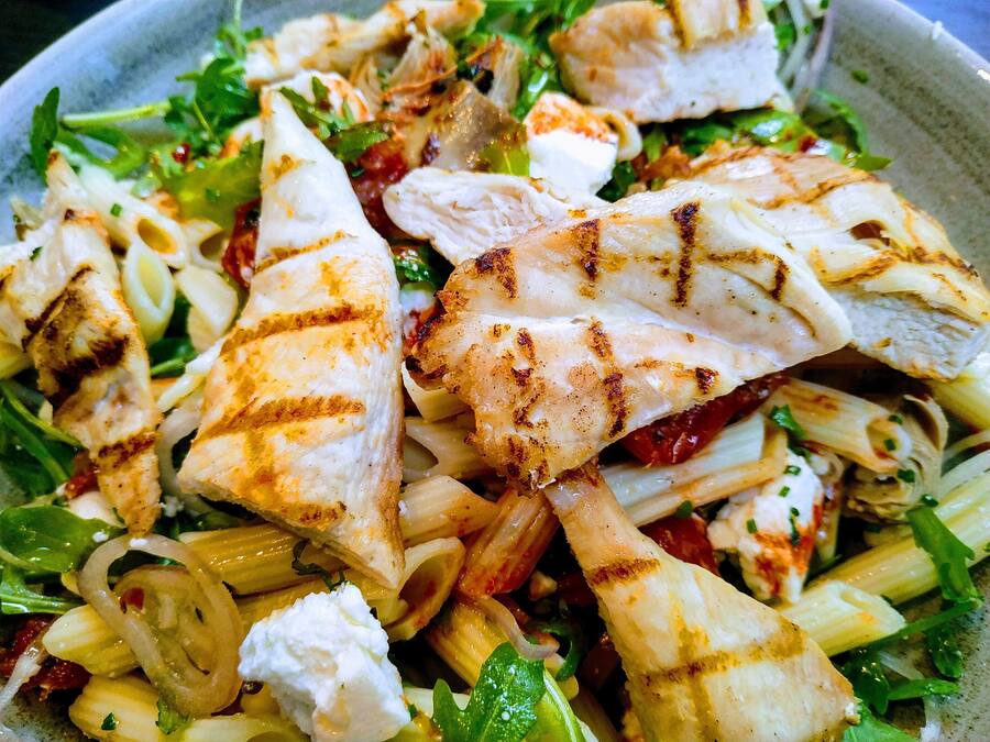 A close-up of a dish with grilled chicken, pasta, and vegetables.