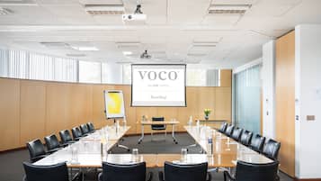 A conference room with a long table, black chairs, a projector screen, and a presentation screen.