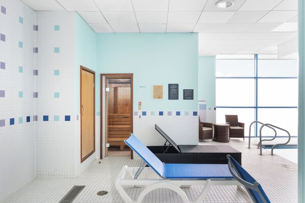 A swimming pool area with a sun lounger, a door leading to a changing room, and a window with a view.