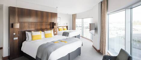 A hotel room with a large bed, a smaller bed, a desk, a chair, a TV, and a large window with a view of the city.