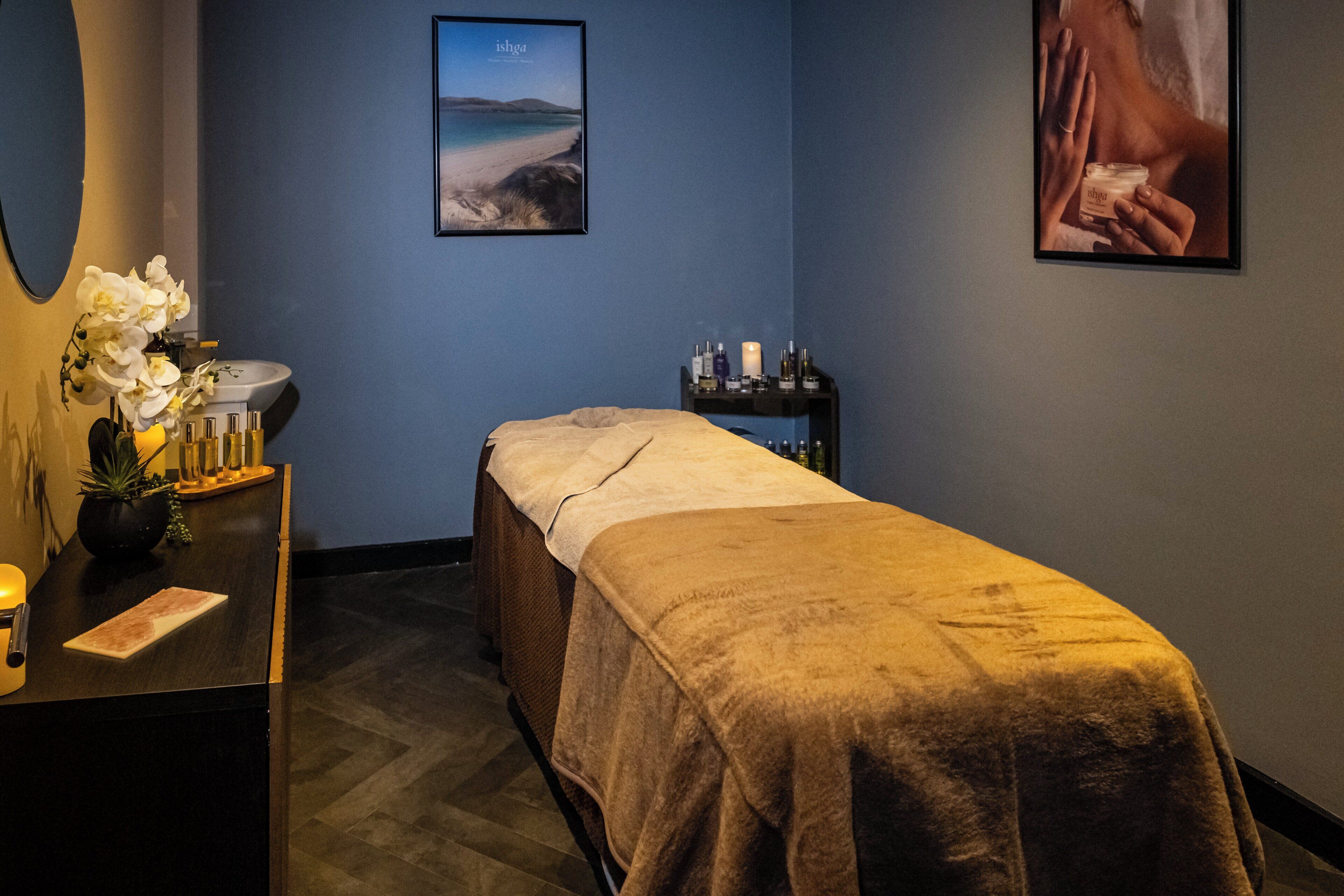 A room with a massage table, a sink, a mirror, and a shelf with bottles.