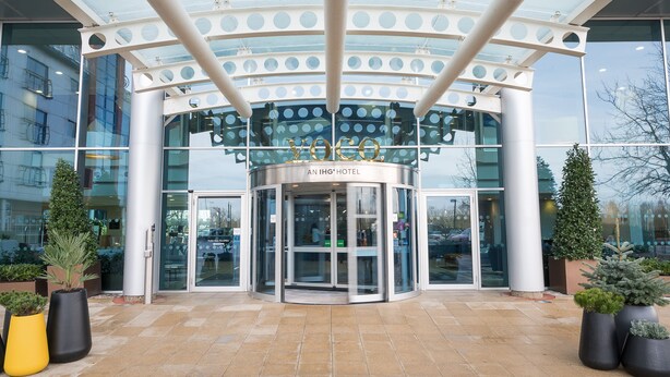 A hotel entrance with a revolving door, glass facade, and potted plants.