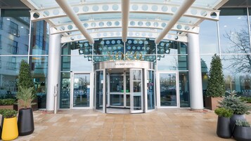 A hotel entrance with a revolving door, glass facade, and potted plants.
