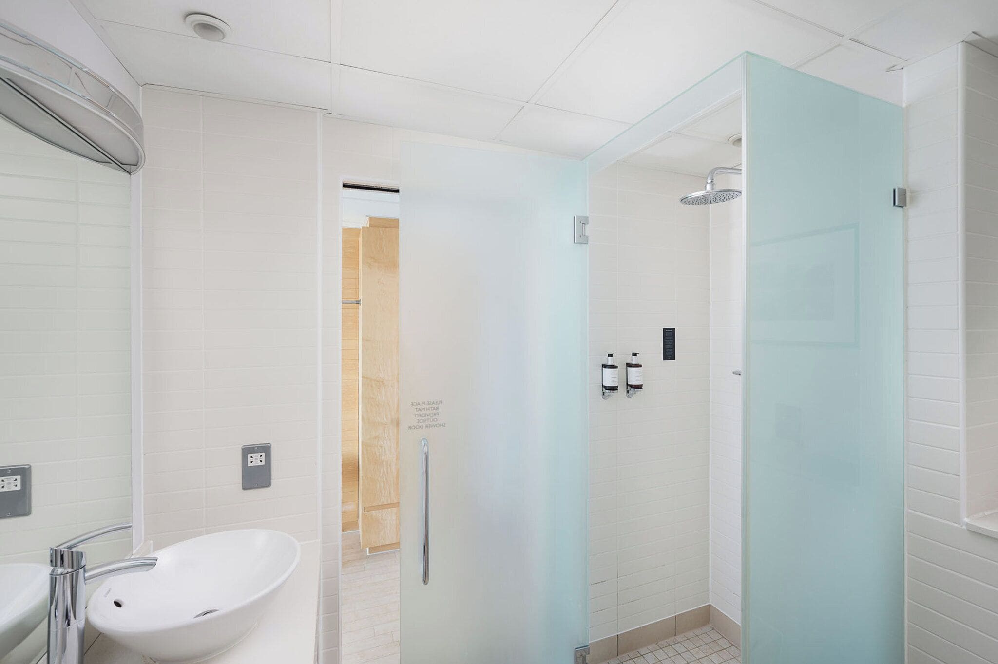 A modern bathroom with a white sink, a glass shower enclosure, and a frosted glass door.