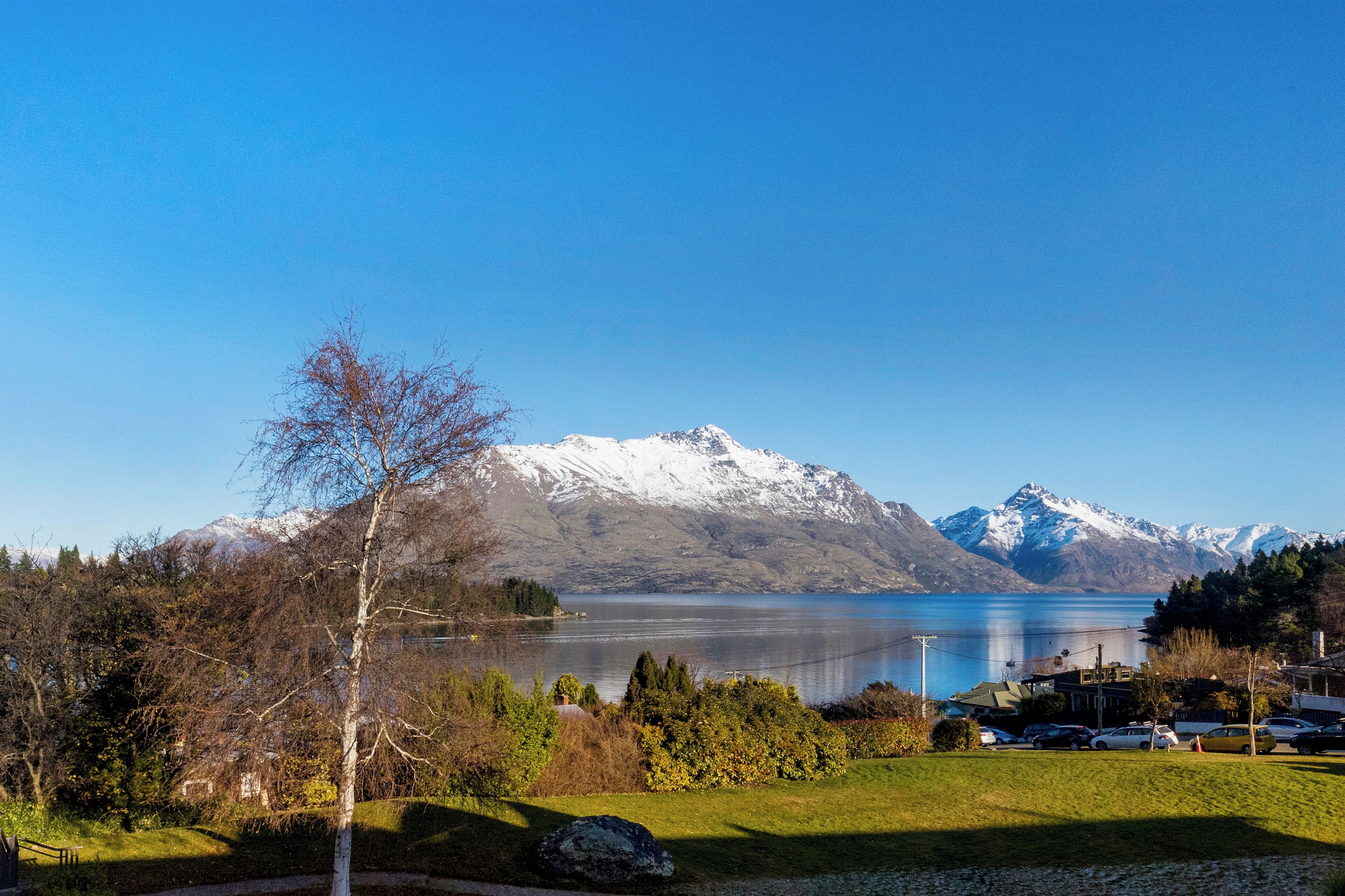 Une vue sur le lac, avec des montagnes en arrière-plan, une zone herbeuse et des voitures garées.