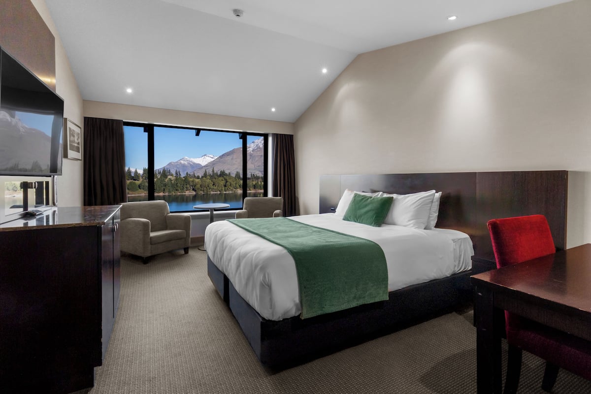 Een hotelkamer met een bed, een bureau, een stoel en uitzicht op een berg en een meer.