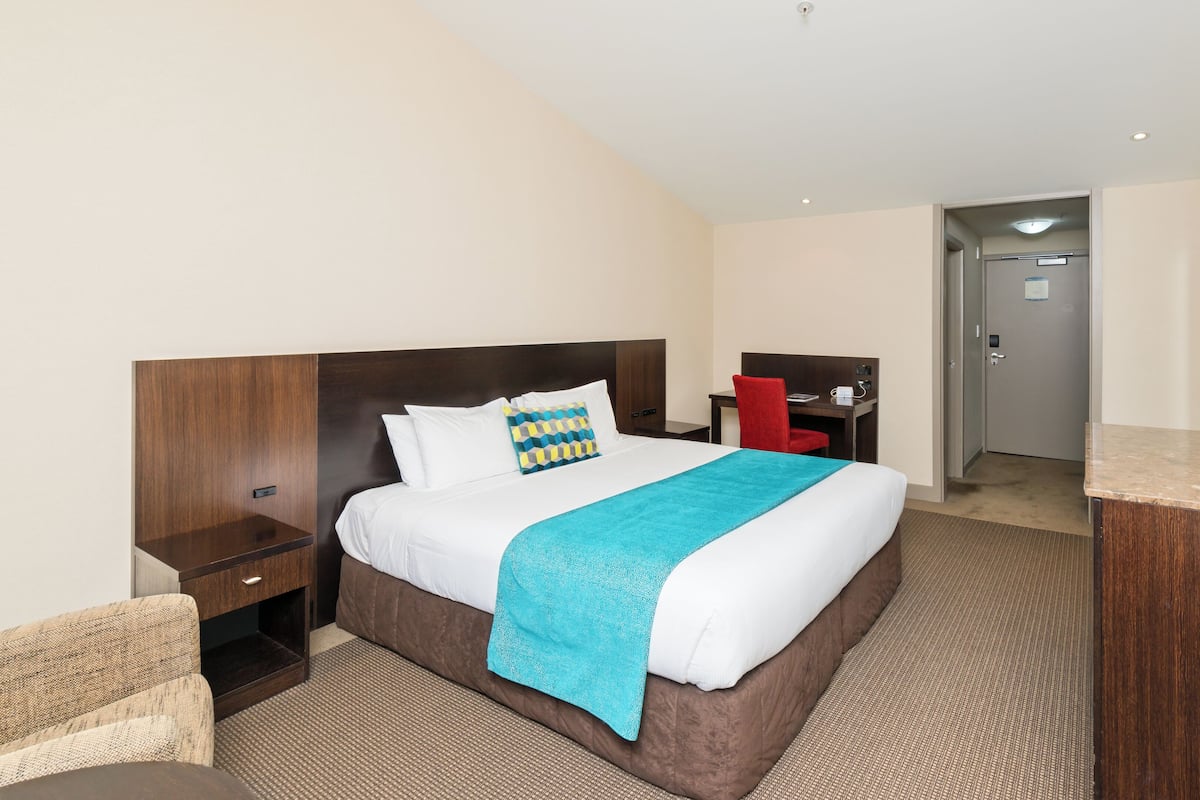 Een hotelkamer met een groot bed, een bureau, een stoel, een televisie en een minibar.