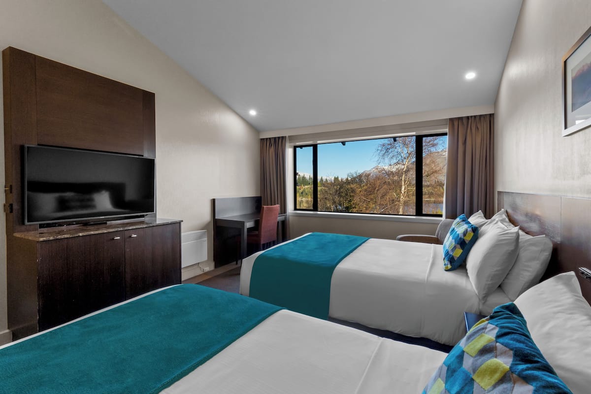 Een hotelkamer met twee bedden, een televisie, een bureau en een raam met uitzicht op bomen.
