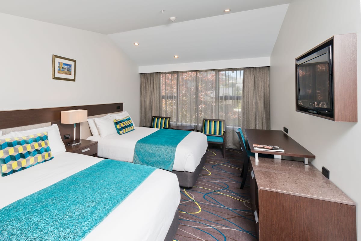 Hotelkamer met twee bedden, een bureau, een stoel, een televisie en een raam met gordijnen.