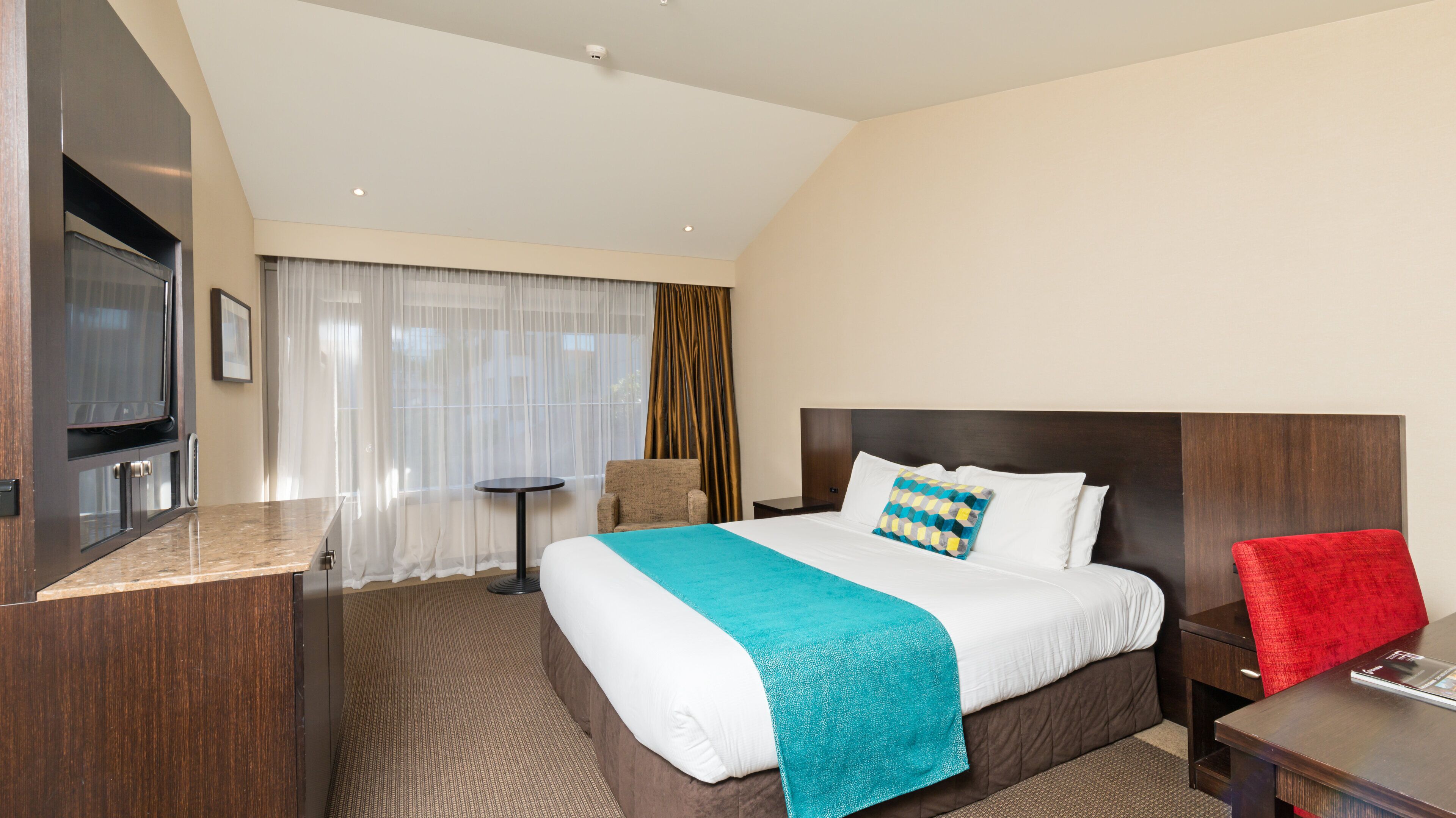 A hotel room with a large bed, a TV, a small table, a chair, and a desk.