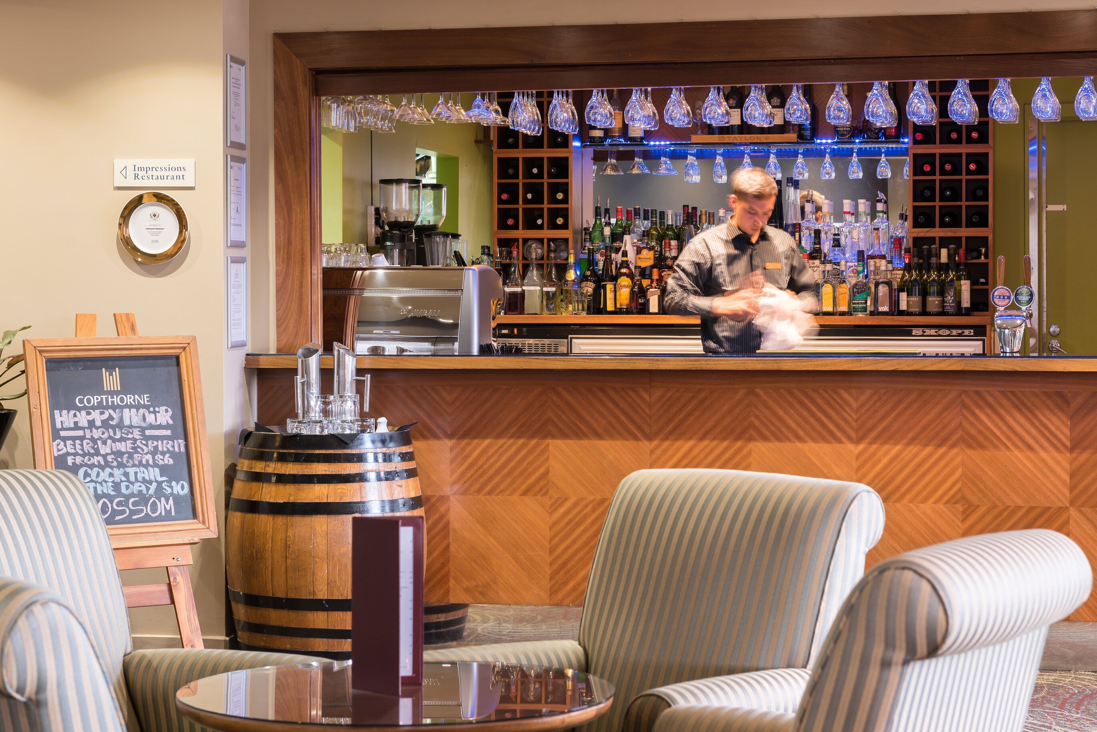 A bar area with a bartender, a wooden bar counter, and a seating area with striped chairs.