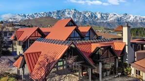 A modern building with a distinctive red roof and large windows, set against a backdrop of snow-capped mountains.