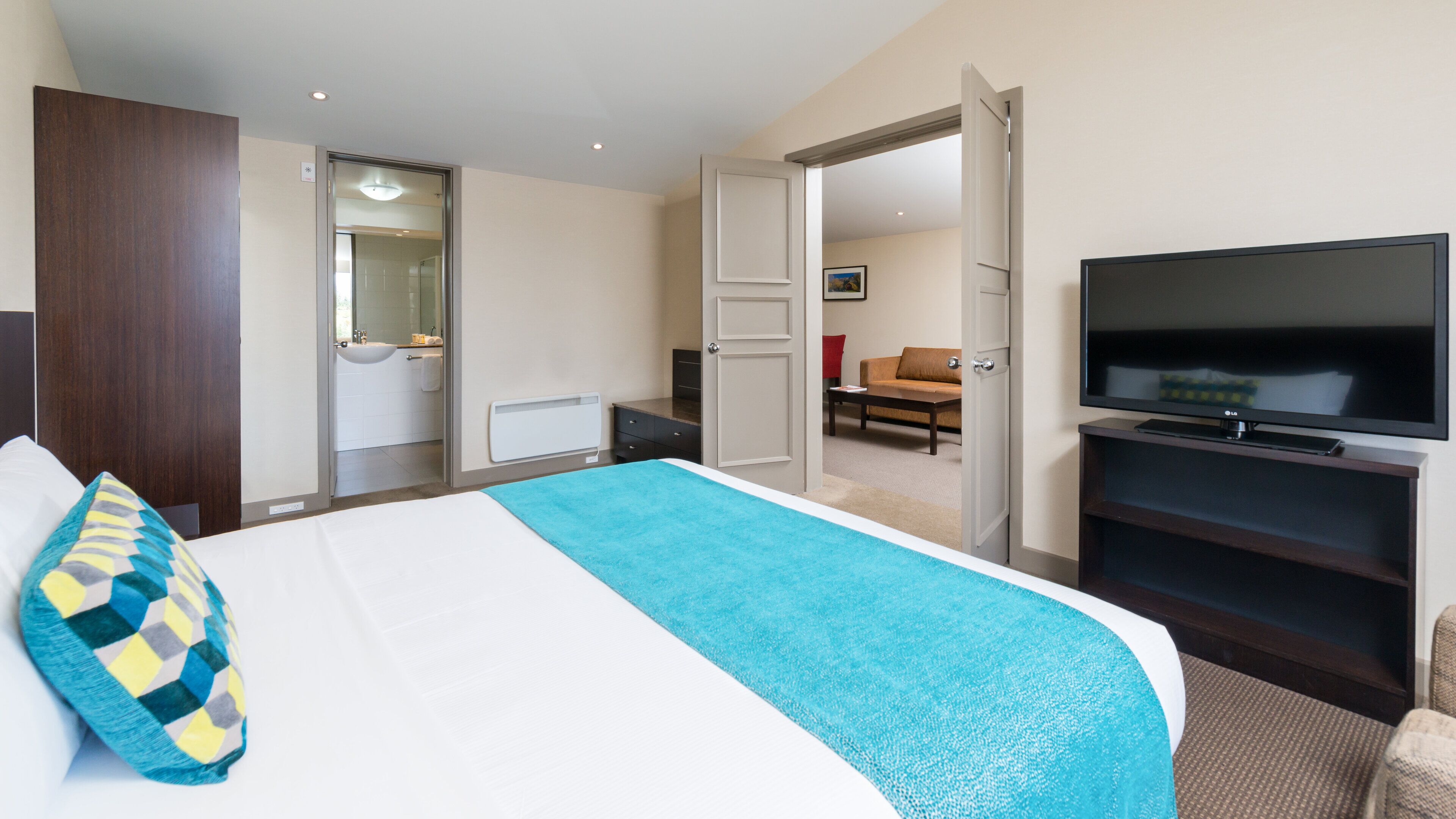 A hotel room with a bed, a TV, a bathroom, and a seating area.