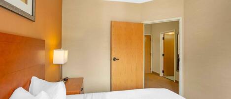 A hotel room with a bed, a nightstand, a lamp, and a wooden door leading to another room.