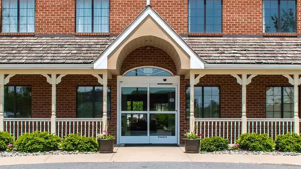 A brick building with a central entrance, large windows, and a porch with white railings. - Extended Stay America Suites Lancaster County (Mountville)